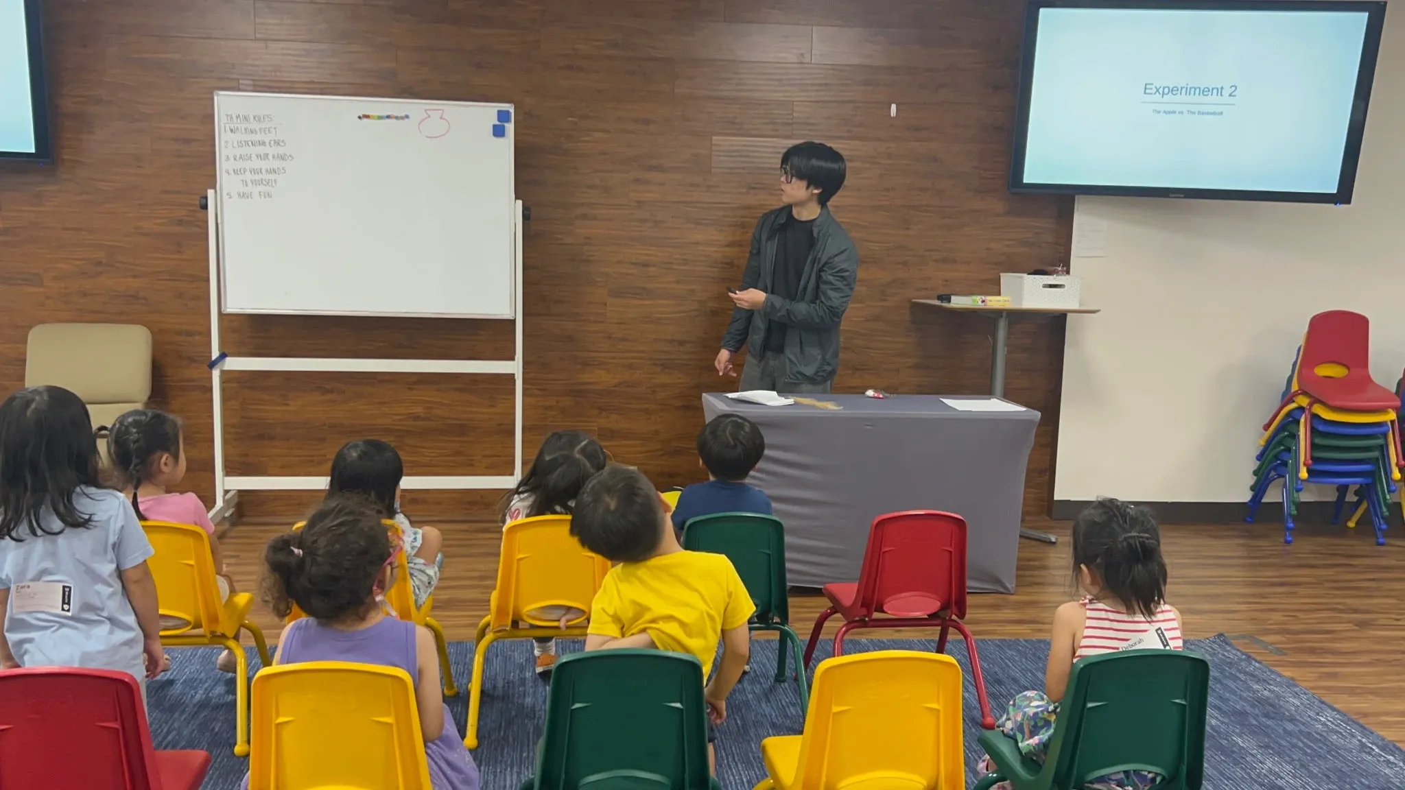 Students seated on colorful chairs listen as Jack Lee introduces the next experiment.