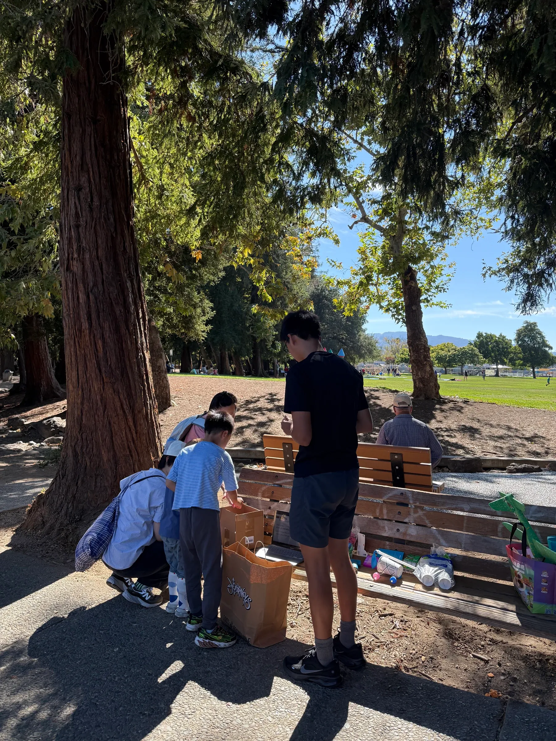 Edward Pan sets up balloon-powered cars with students and a parent beside a bench at Serra Park.
