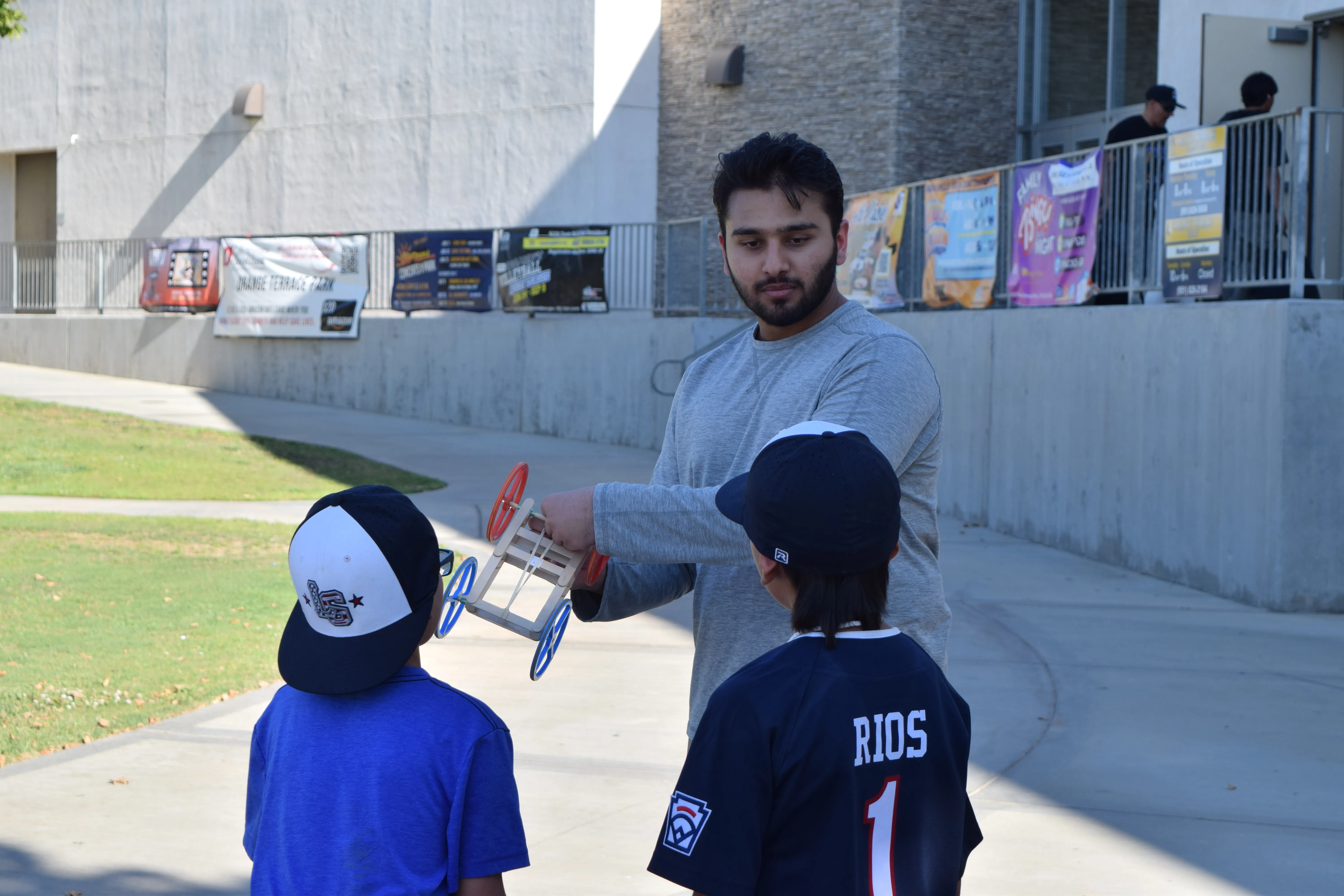 A STEM Inspire mentor demonstrates a rubber band car to two children.